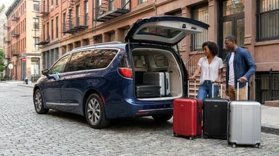 Three adults loading three suitcases into a car rental on a New York street
