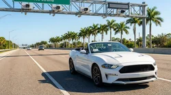 White car rental driving under an electronic toll booth on a sunny Florida highway