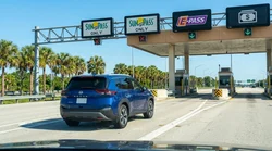 White car rental driving through an electronic toll plaza on a sunny Florida highway