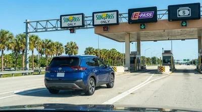 White car rental driving through an electronic toll plaza on a sunny Florida highway