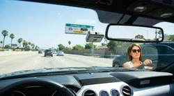 A modern car rental driving under a FasTrak express lane sign on a sunny California highway