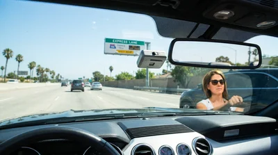 A modern car rental driving under a FasTrak express lane sign on a sunny California highway