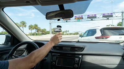 White car rental passing under an electronic toll gantry on a sunny Florida highway
