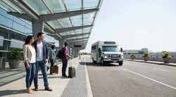 Travelers with luggage walking toward a car rental shuttle bus at LaGuardia Airport in New York