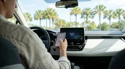 Driver using a smartphone near the dashboard screen of a car rental parked by palm trees in Orlando