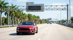 Silver car rental driving on a sunlit express lane highway with the downtown Miami skyline in the background
