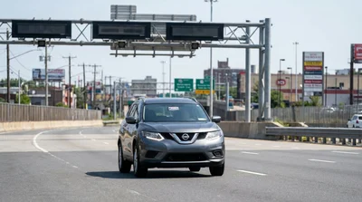 Silver car rental driving through an electronic toll booth on a New York highway