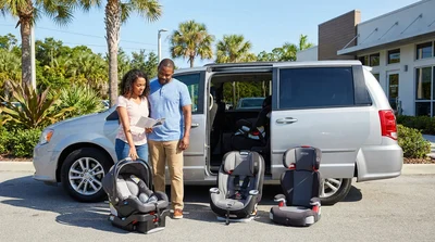 Parent buckling a toddler into a child seat in the back of a car rental in sunny Florida