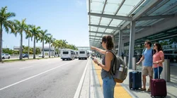 Travelers with luggage walking toward a car hire shuttle bus outside Terminal D at Miami Airport