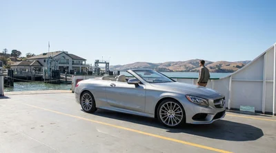 A white car rental parked on an open ferry deck crossing a scenic bay in California