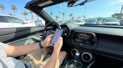Person holding a smartphone near the dashboard screen of a car rental in California