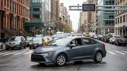 A white car rental driving through congested traffic on a busy New York street with tall buildings