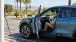 Person using a smartphone beside an electric car rental plugged into a charging station in sunny California