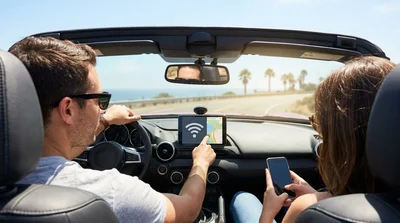 Person using a smartphone inside a modern car rental parked along a scenic coastal highway in California