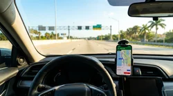 Person holding a smartphone with a map open outside a Florida car rental lot on a sunny day