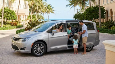 A family packing luggage and a child seat into a white SUV car rental parked by palm trees in Miami