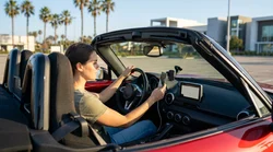 Driver adjusting a hands-free sat nav on the dashboard of a car rental along a sunny California highway