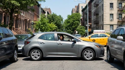 Small car rental parallel parked on a busy New York street with tall skyscrapers in the background