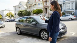 Person holding a smartphone next to a car rental parked on a hilly street in San Francisco