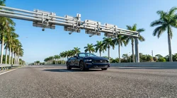 Silver car rental passing under an overhead toll camera gantry on a sunny Florida highway
