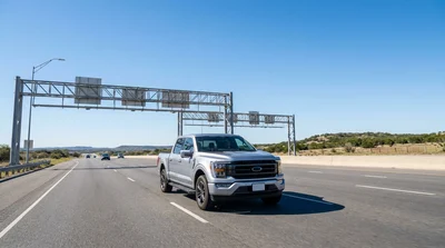 Person driving a car rental past an electronic toll sign on a sunny Texas highway