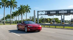 White car rental driving past palm trees on a sunny Miami toll road