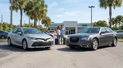 Standard and full-size car hire vehicles parked side by side on a sunny Florida street lined with palm trees