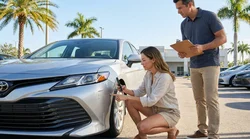 Person taking a photo of a scratch on a car rental in a sunny Florida parking lot