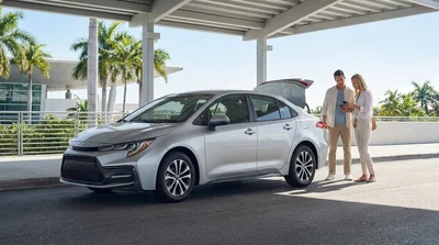 Traveler with luggage standing next to a car hire vehicle outside a Miami airport terminal