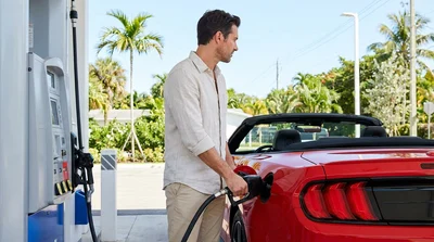 Person filling a white car rental with gas at a sunny Miami gas station with palm trees
