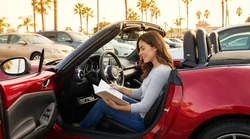 Driver checking documents in the open glovebox of a California car rental parked on a sunny street