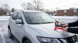 Person using an ice scraper to clear the windshield of a car rental in snowy Pennsylvania