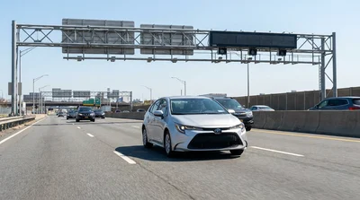 Silver car rental driving on a New York highway approaching a toll booth