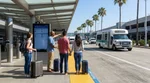 Passengers with luggage boarding a car rental shuttle bus outside the LAX airport terminal in Los Angeles