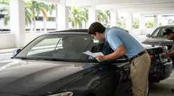Person inspecting the front license plate of a car rental in a sunny Miami parking lot