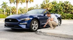 Driver inspecting the front bumper and wheel of a car rental parked on a sunny Florida street