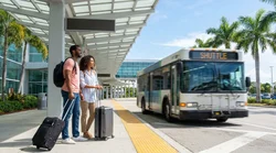 Travelers waiting with luggage for a car hire shuttle bus outside Terminal E at Miami Airport