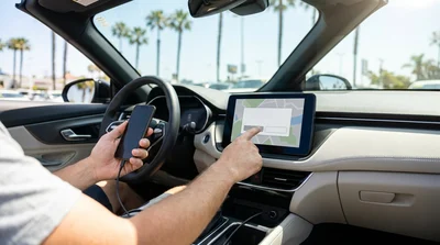 Driver using an Apple CarPlay dashboard screen in a car rental parked on a sunny street in California