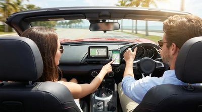 Smartphone displaying a map mounted on the dashboard of a car rental on a sunny Miami street