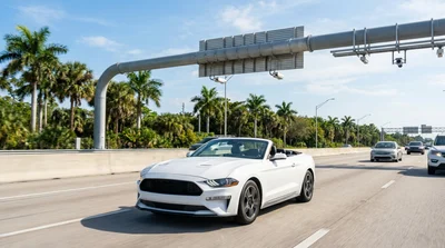White car rental driving under an electronic toll gantry on a sunny Florida highway