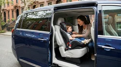 Parent buckling a child into a safety seat inside a car rental parked on a New York street