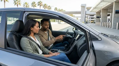 Driver adjusting the dashboard display inside a car rental parked along a scenic California highway