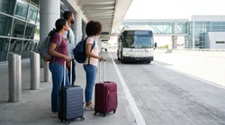 Traveler with luggage waiting to board a car rental shuttle bus outside a New York terminal