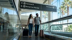 Traveler rolling luggage past directional signs for car rental pickup in Orlando airport Terminal B