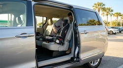 Child safety seat installed in the back of a car rental with sunny Florida palm trees visible outside the window