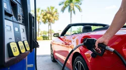Petrol pump nozzle inserted into a car rental at a sunny Florida gas station