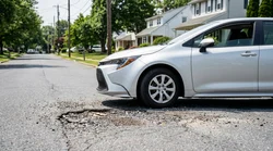 A modern car rental driving on a cracked road near a large pothole in Pennsylvania