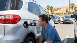 Person checking the fuel cap of a car rental at a sunny gas station in California