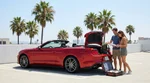Person loading luggage into a car rental trunk under bright palm trees in Los Angeles