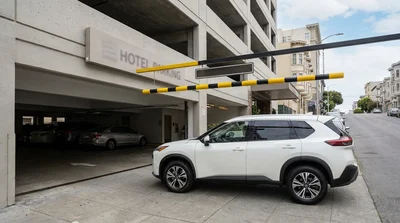 A white car rental driving under a height limit bar at a San Francisco hotel parking garage